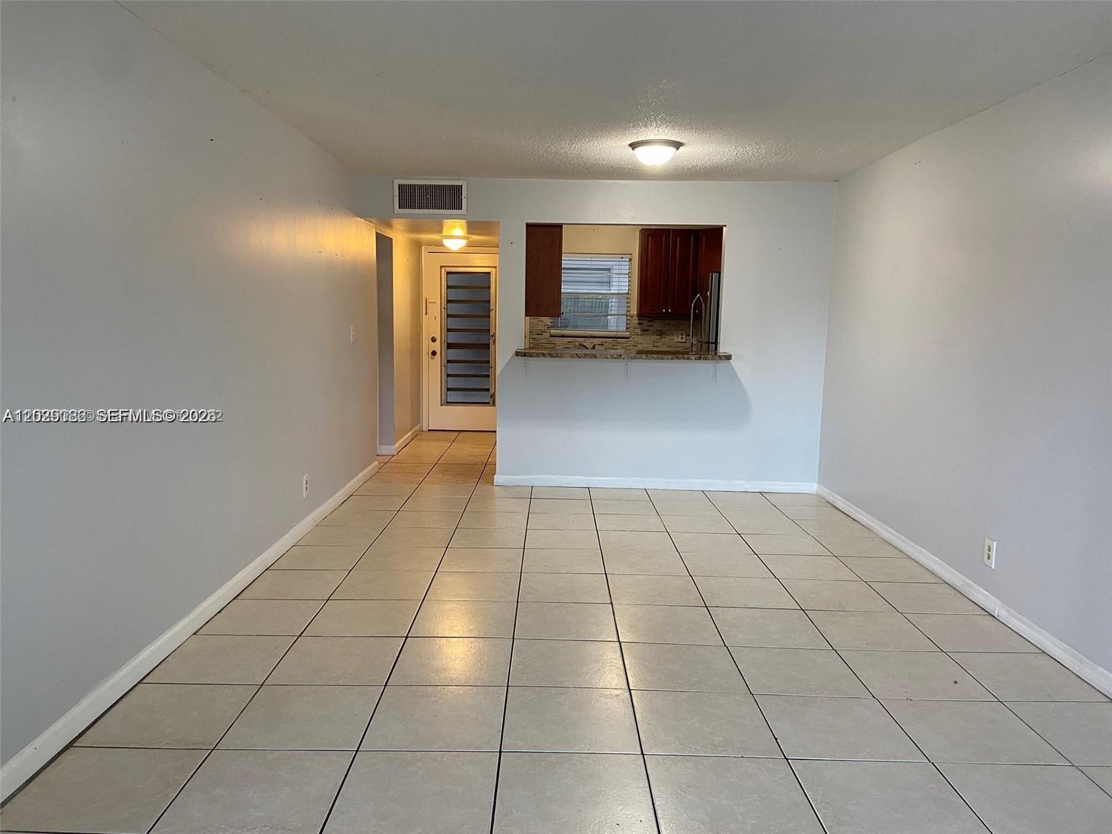 An empty room with light-colored tile flooring features a kitchen pass-through window and entryway — 6501 Winfield Blvd # 26, Margate FL 33063, MARGATE, FL