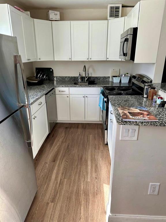 A kitchen features white cabinets, granite countertops, stainless steel appliances, and wood-look flooring — 2451 OAK PARK WAY UNIT 120, ORLANDO, FL