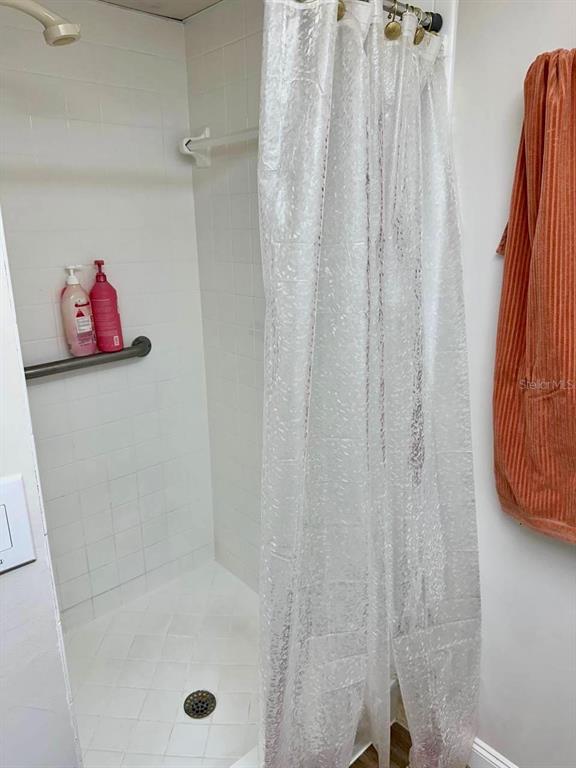 A walk-in shower features white tiled walls, a grab bar, and a clear plastic curtain — 2451 OAK PARK WAY UNIT 120, ORLANDO, FL