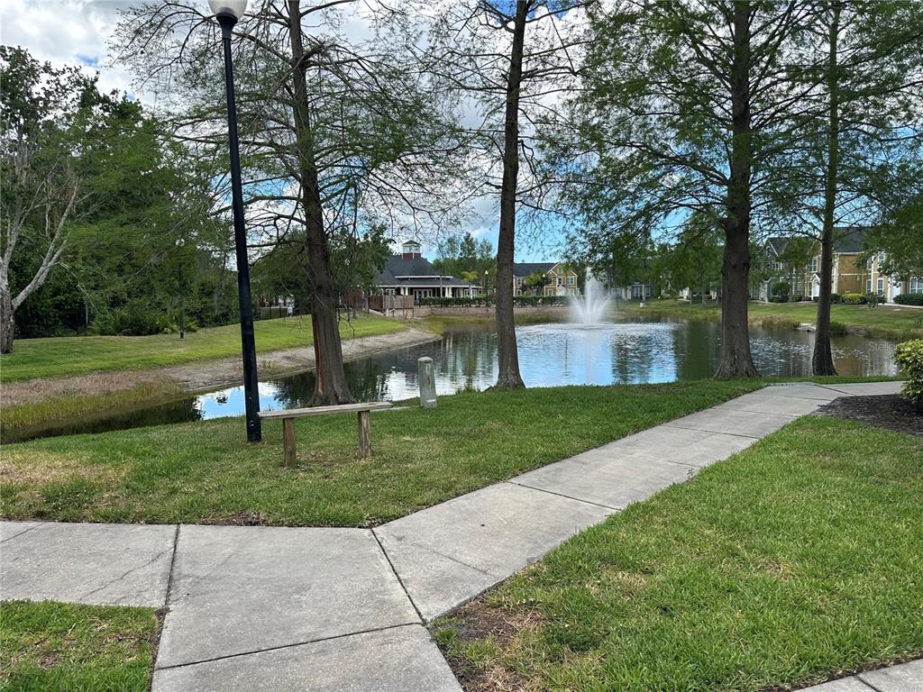 A concrete walkway leads toward a pond with a fountain and surrounding trees — 5601 ROSEHILL ROAD UNIT 201, SARASOTA, FL