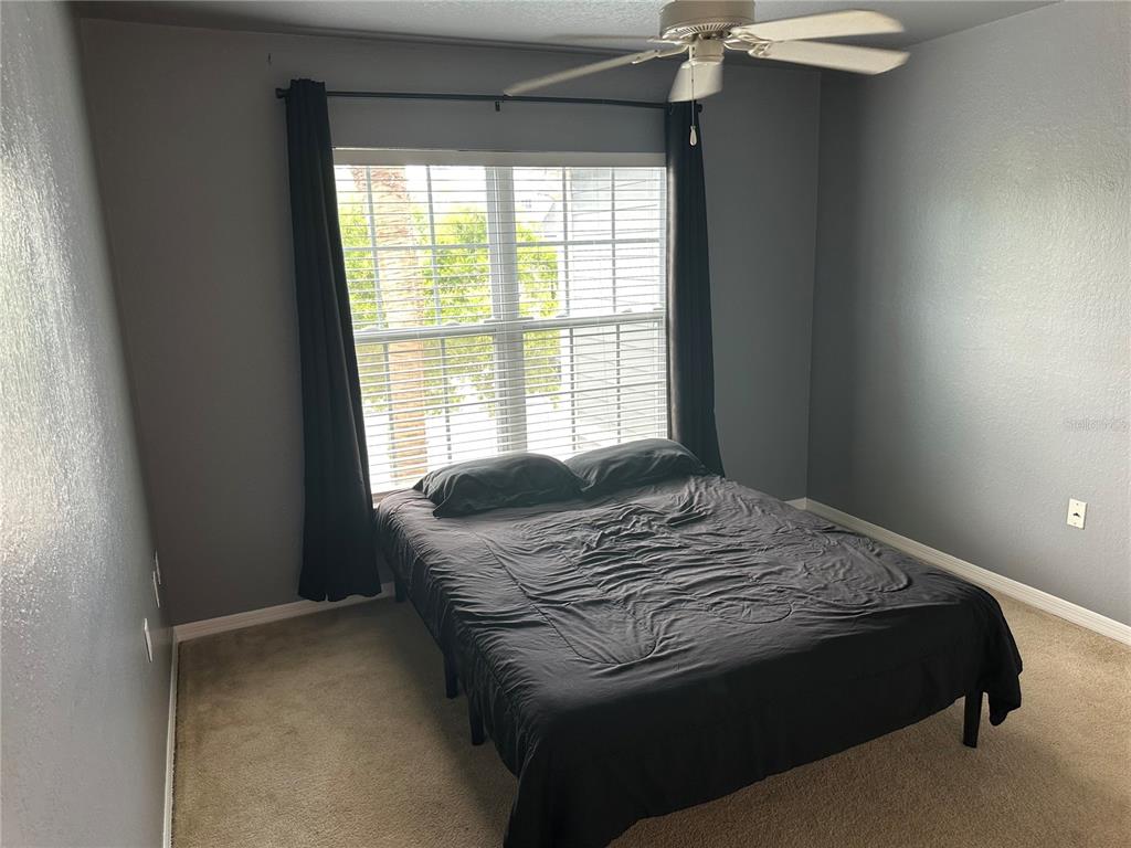 A bedroom with gray walls, beige carpet, a ceiling fan, and a bed with black bedding — 5601 ROSEHILL ROAD UNIT 201, SARASOTA, FL