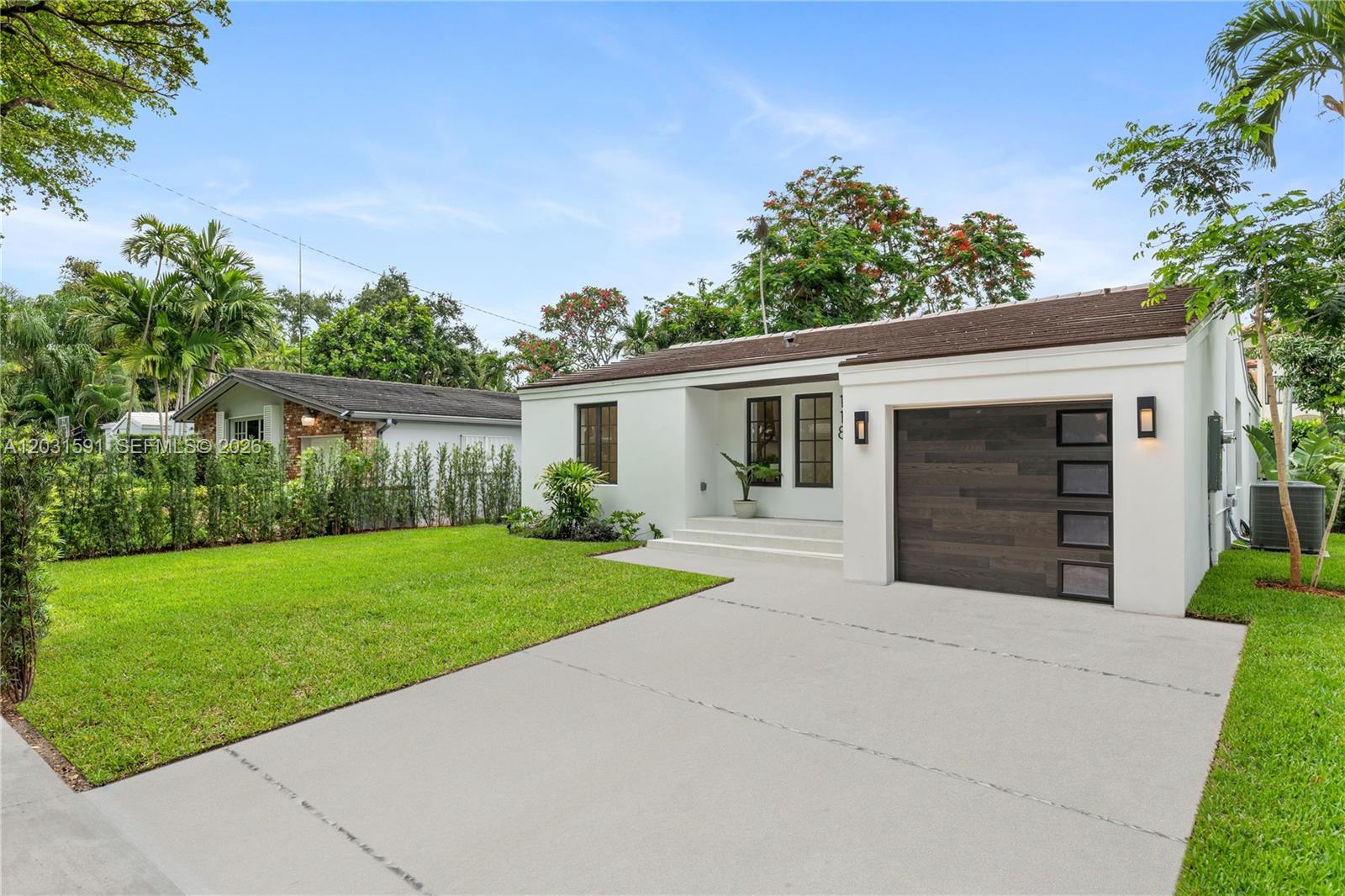 A white single-story house features a dark wood garage door and a concrete driveway — 118 Sarto Ave, Coral Gables FL 33134, CORAL GABLES, FL