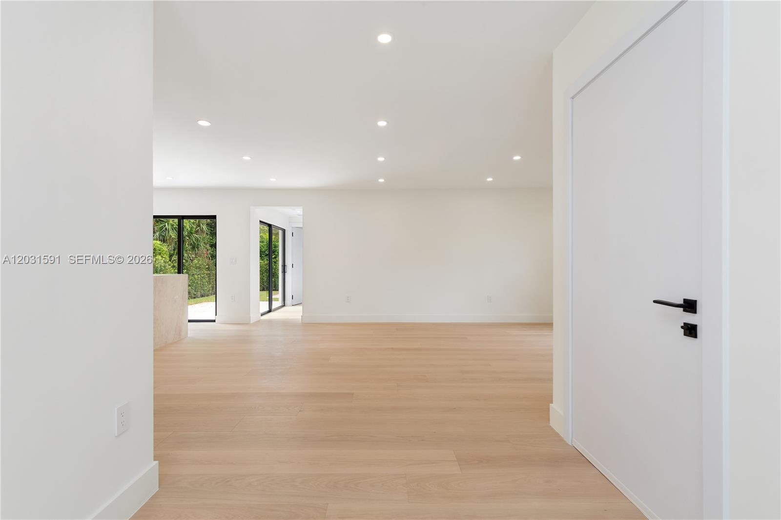 A bright, minimalist room features light wood flooring, white walls, and black-framed glass doors — 118 Sarto Ave, Coral Gables FL 33134, CORAL GABLES, FL