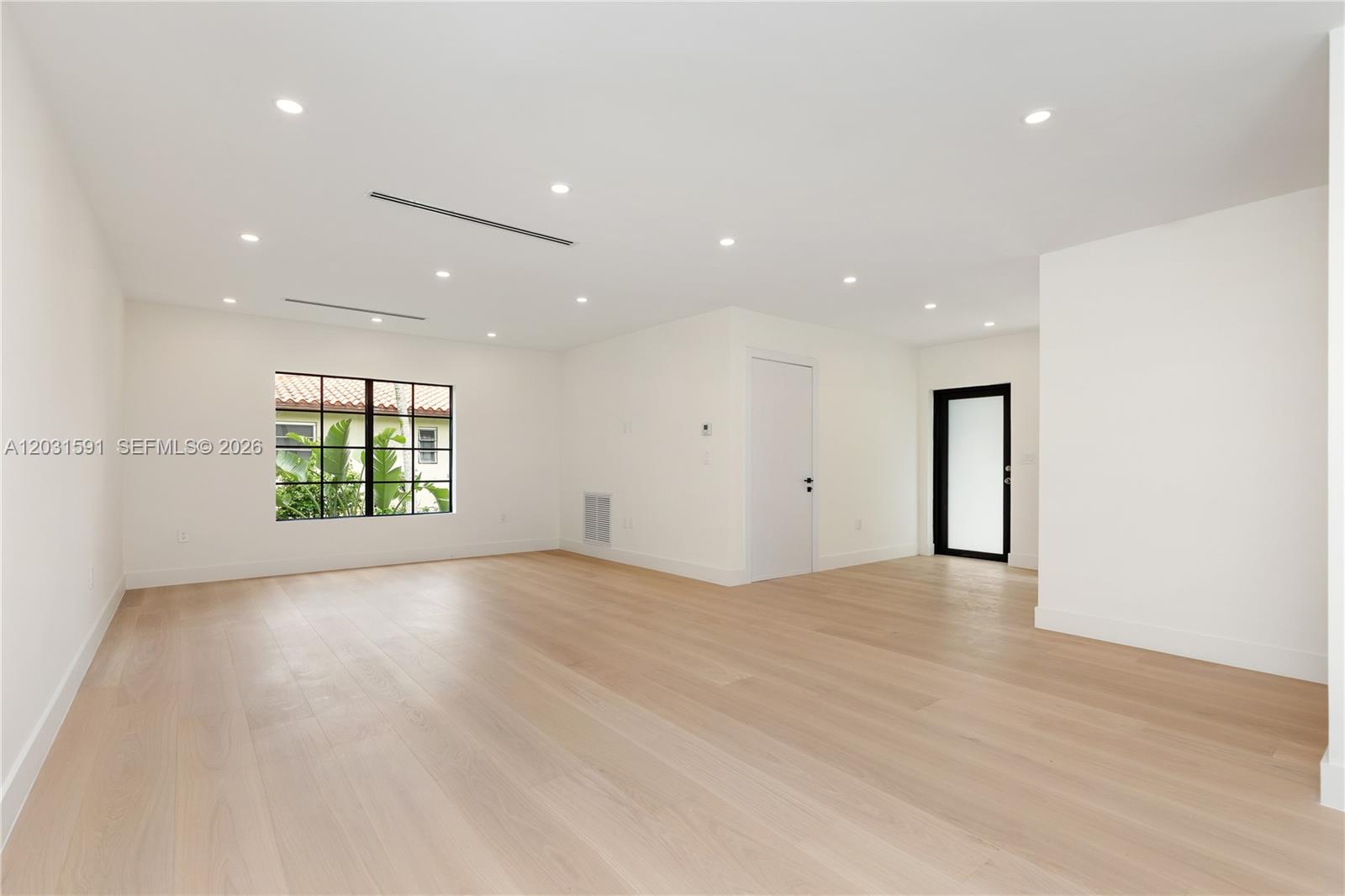 An empty room features light wood flooring, white walls, recessed lighting, and a black-framed window — 118 Sarto Ave, Coral Gables FL 33134, CORAL GABLES, FL
