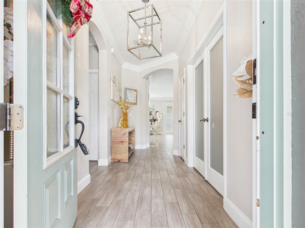 A bright entryway features wood-look tile flooring, a modern lantern pendant light, and arched doorways — 4590 SW 99TH STREET, OCALA, FL