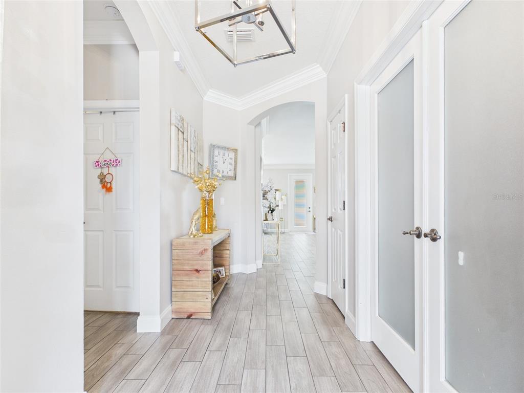 A bright hallway features light wood-look tile flooring, arched doorways, and a modern geometric chandelier — 4590 SW 99TH STREET, OCALA, FL