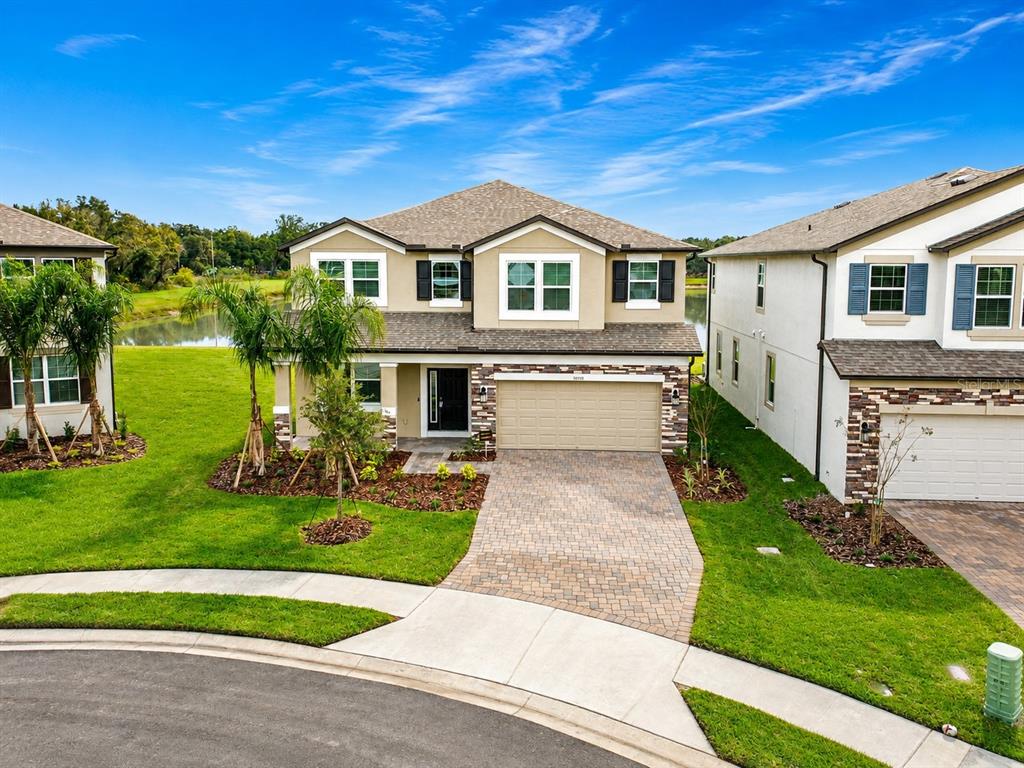 A two-story suburban house with a paved driveway, stone accents, and a view of a pond — 38190 SHALE STONE COURT, ZEPHYRHILLS, FL