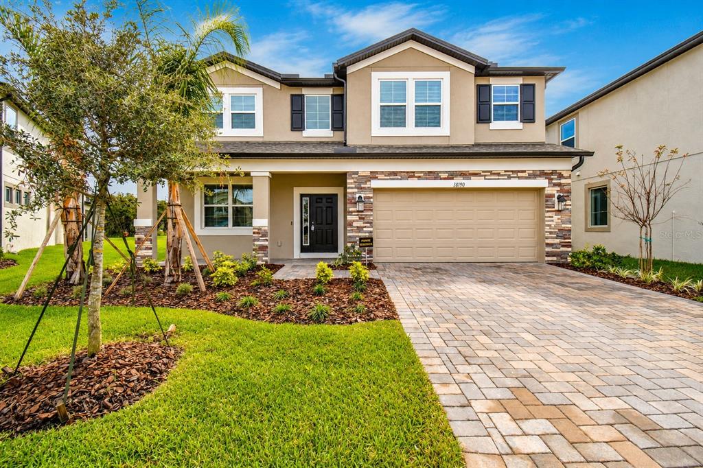 A two-story suburban house features a stone-accented facade, a paved driveway, and a manicured lawn — 38190 SHALE STONE COURT, ZEPHYRHILLS, FL