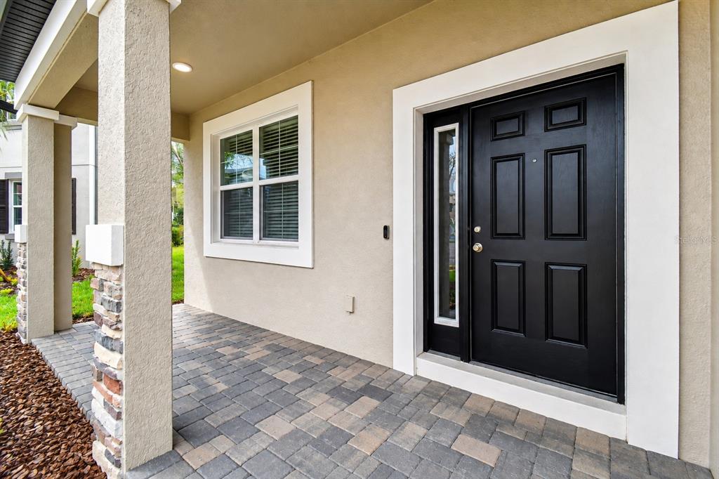A covered front porch features a black door, a window, and stone-accented pillars — 38190 SHALE STONE COURT, ZEPHYRHILLS, FL