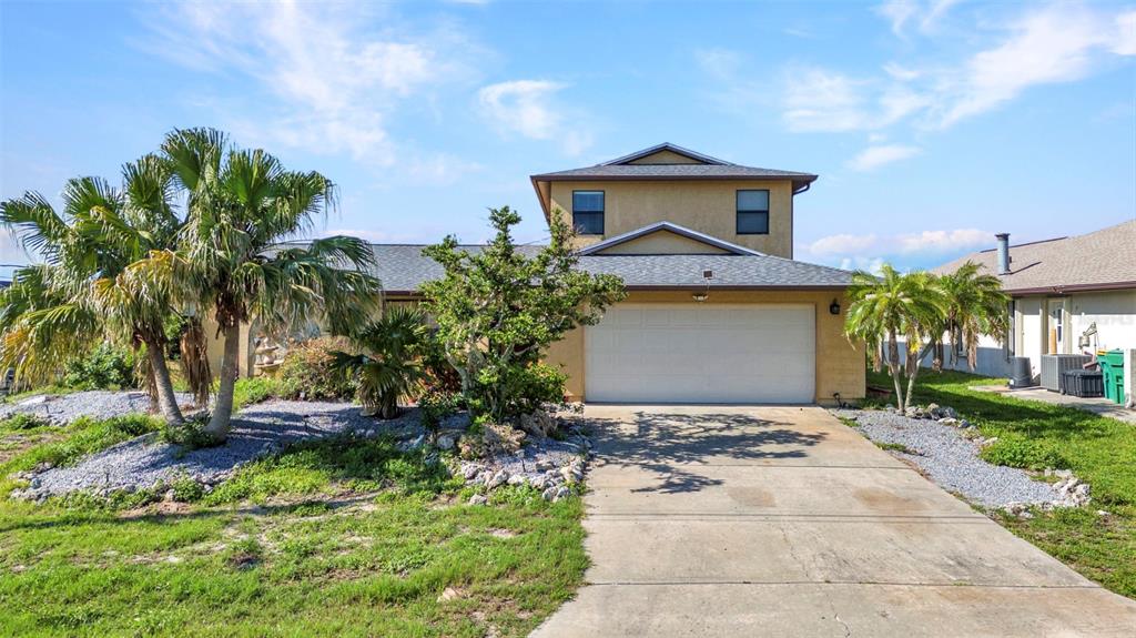 A two-story house with a tan stucco exterior, a white garage door, and palm trees — 18566 ARAPAHOE CIRCLE, PORT CHARLOTTE, FL