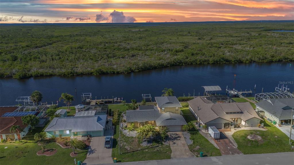 An aerial view shows three waterfront houses along a canal with a sunset sky background — 18566 ARAPAHOE CIRCLE, PORT CHARLOTTE, FL