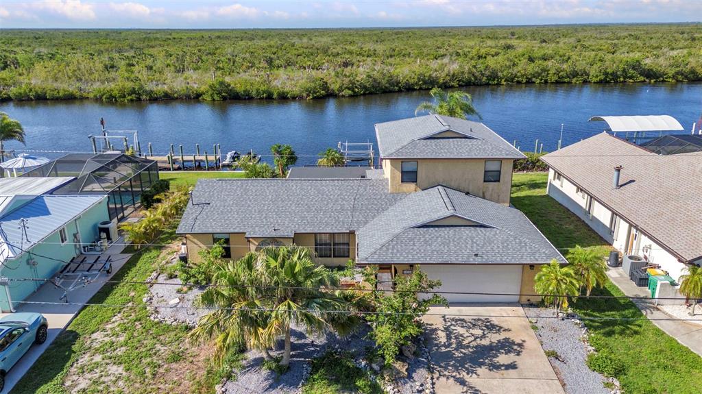 An aerial view shows a two-story house with a gray roof next to a canal — 18566 ARAPAHOE CIRCLE, PORT CHARLOTTE, FL