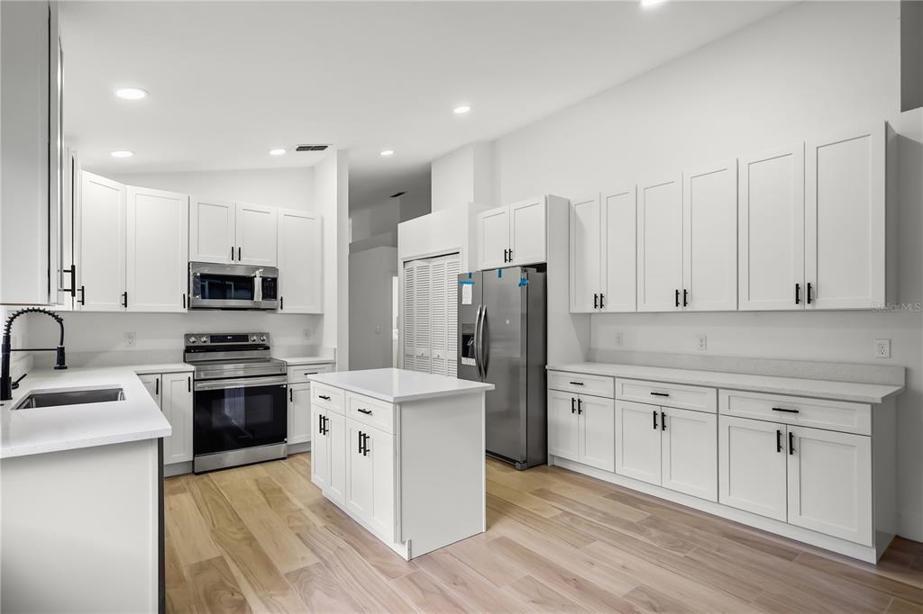 A modern kitchen features white cabinets, stainless steel appliances, a center island, and wood flooring — 14510 QUAIL TRAIL CIRCLE, ORLANDO, FL