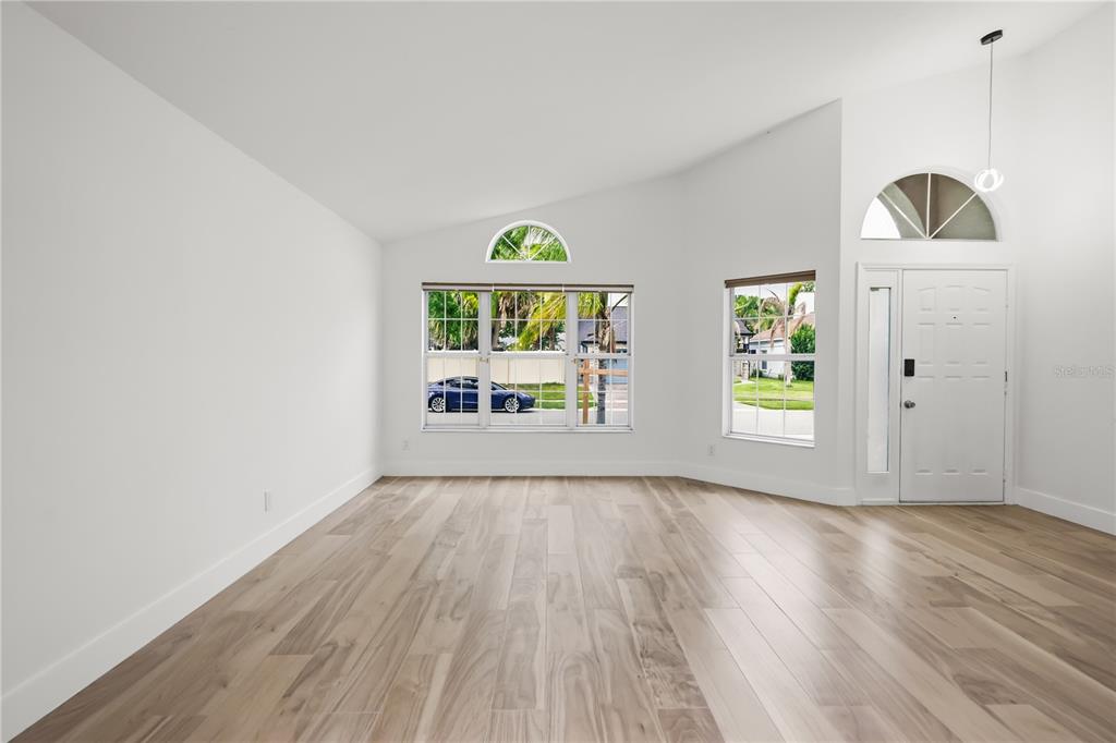 A bright, empty living room features vaulted ceilings, light wood-look flooring, and a front door — 14510 QUAIL TRAIL CIRCLE, ORLANDO, FL