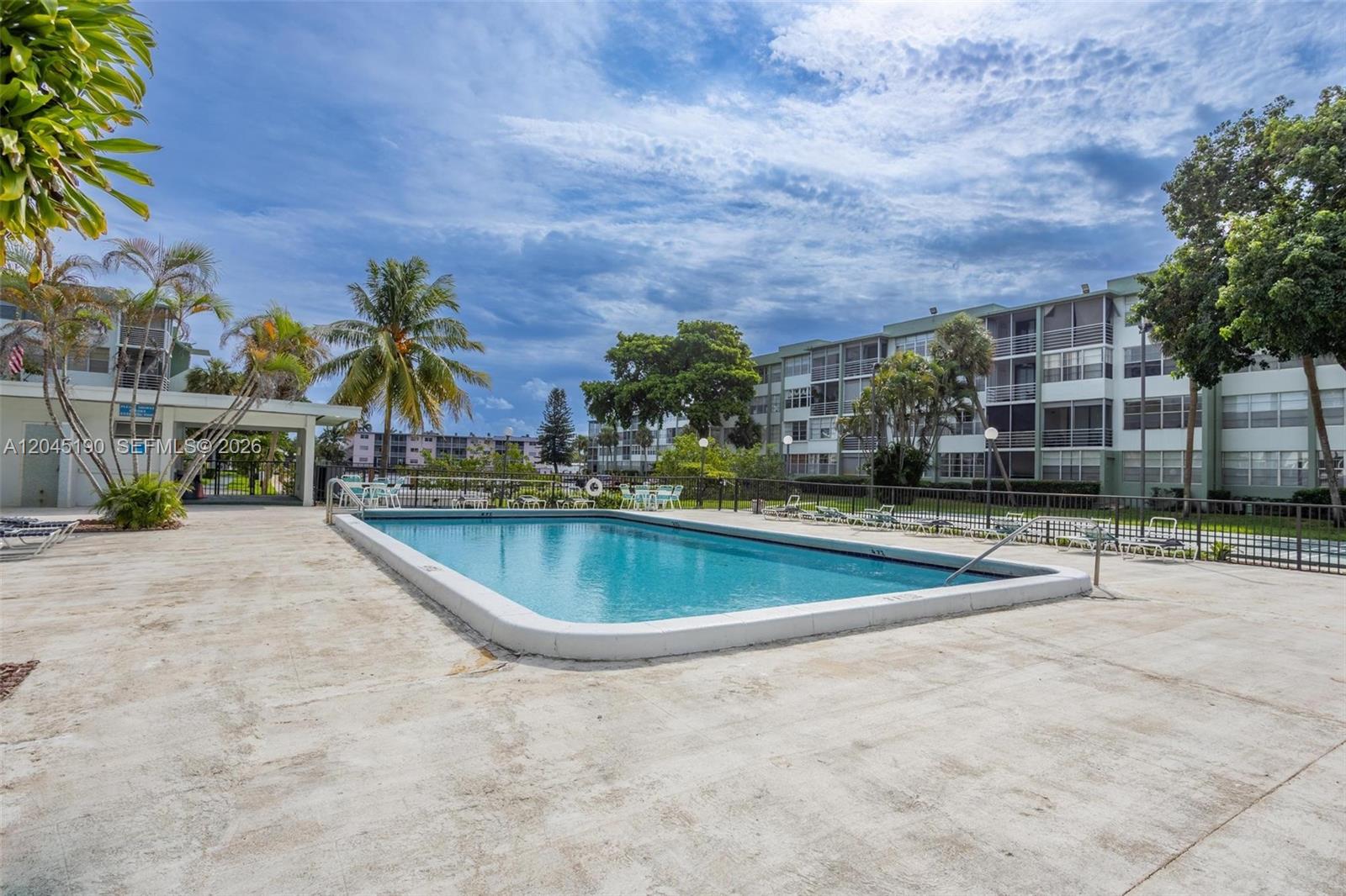 A rectangular swimming pool sits on a concrete deck surrounded by palm trees and buildings — 2771 Taft St # 104, Hollywood FL 33020, HOLLYWOOD, FL