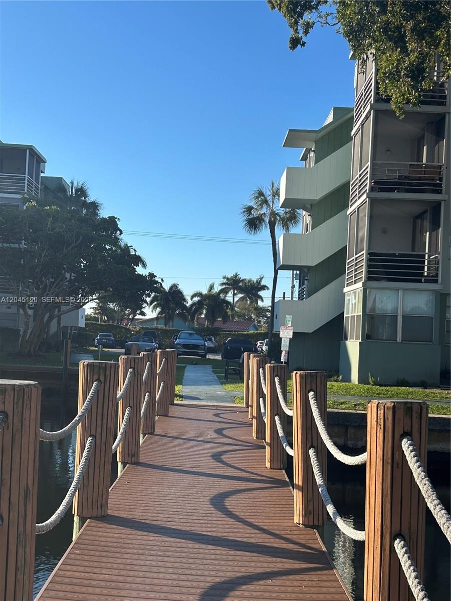 A wooden dock with rope railings leads toward a multi-story apartment building and parking area — 2771 Taft St # 104, Hollywood FL 33020, HOLLYWOOD, FL