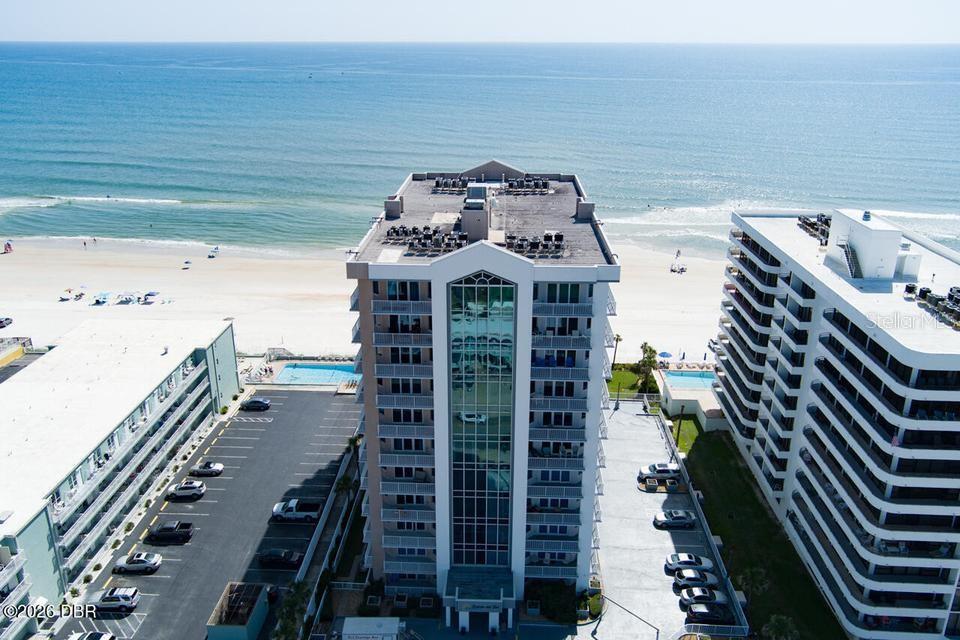 An aerial view shows a tall beachfront condominium building surrounded by parking lots and the ocean — 3737 S ATLANTIC AVENUE UNIT 401, DAYTONA BEACH SHORES, FL