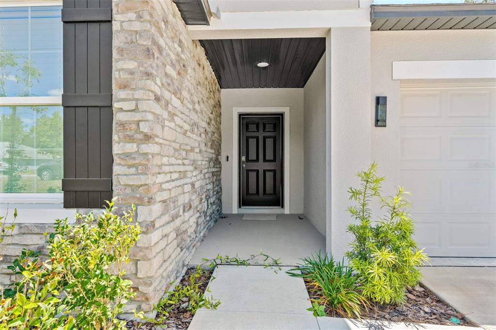 The exterior of a house features a stone facade, a black front door, and landscaping — 13296 THRASHER AVENUE, WEEKI WACHEE, FL