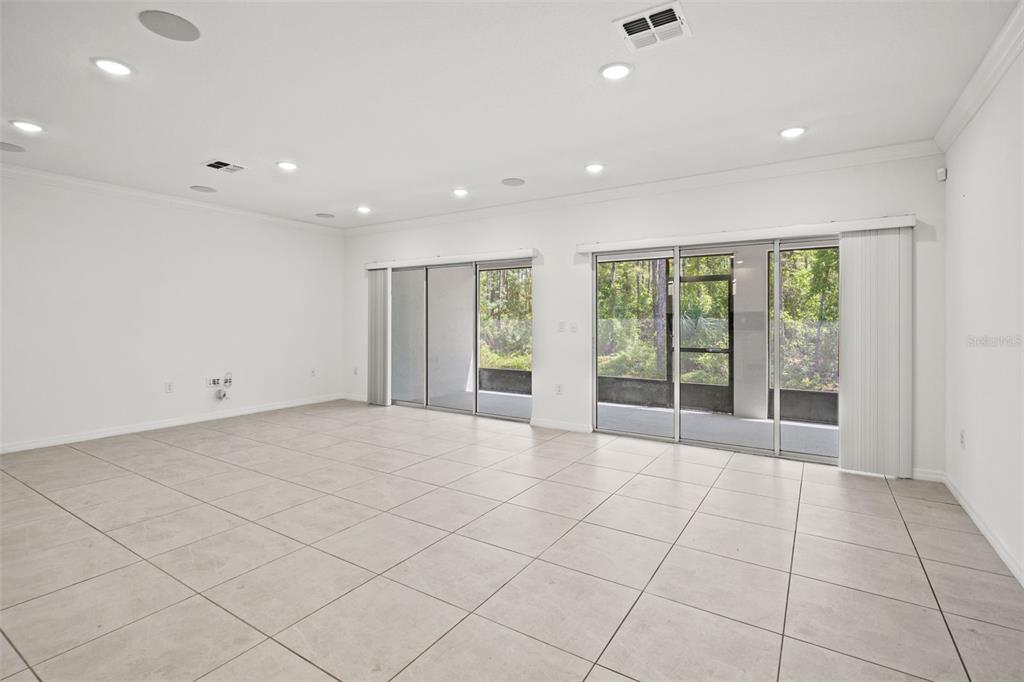 A spacious, empty room features light-colored tile flooring, recessed lighting, and large sliding glass doors — 13296 THRASHER AVENUE, WEEKI WACHEE, FL