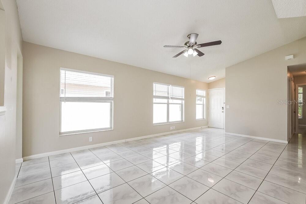 A bright, empty living room features white tile flooring, neutral walls, and a ceiling fan — 9710 RED CLOVER AVENUE, ORLANDO, FL