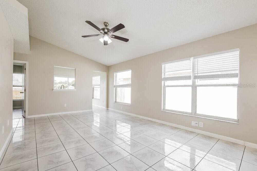 A bright, empty room features light-colored tile flooring, a vaulted ceiling, and large windows — 9710 RED CLOVER AVENUE, ORLANDO, FL