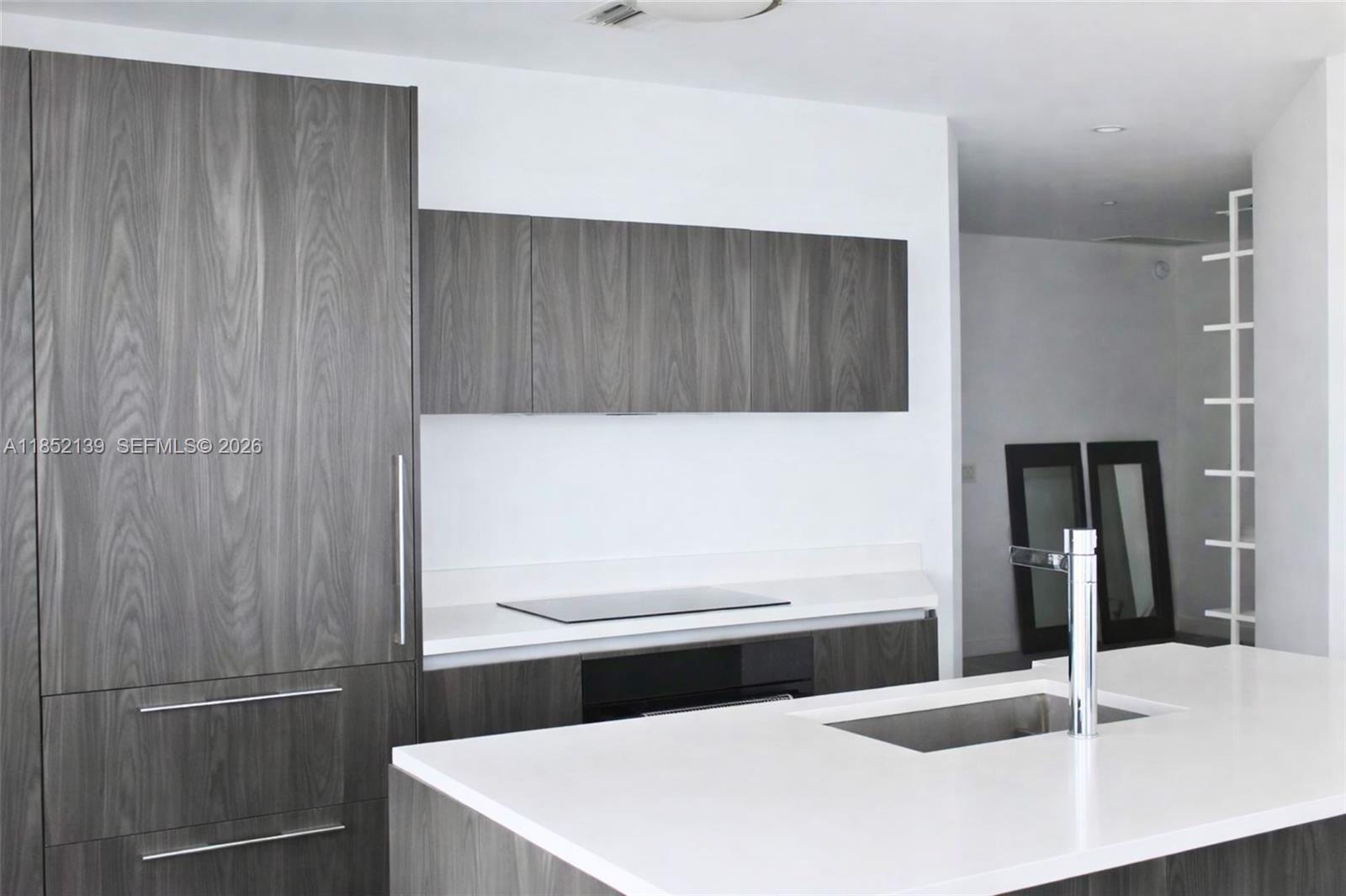 A modern kitchen features dark wood-grain cabinetry, white countertops, and a central island with sink — 480 NE 31st St # 3301, Miami FL 33137, MIAMI, FL