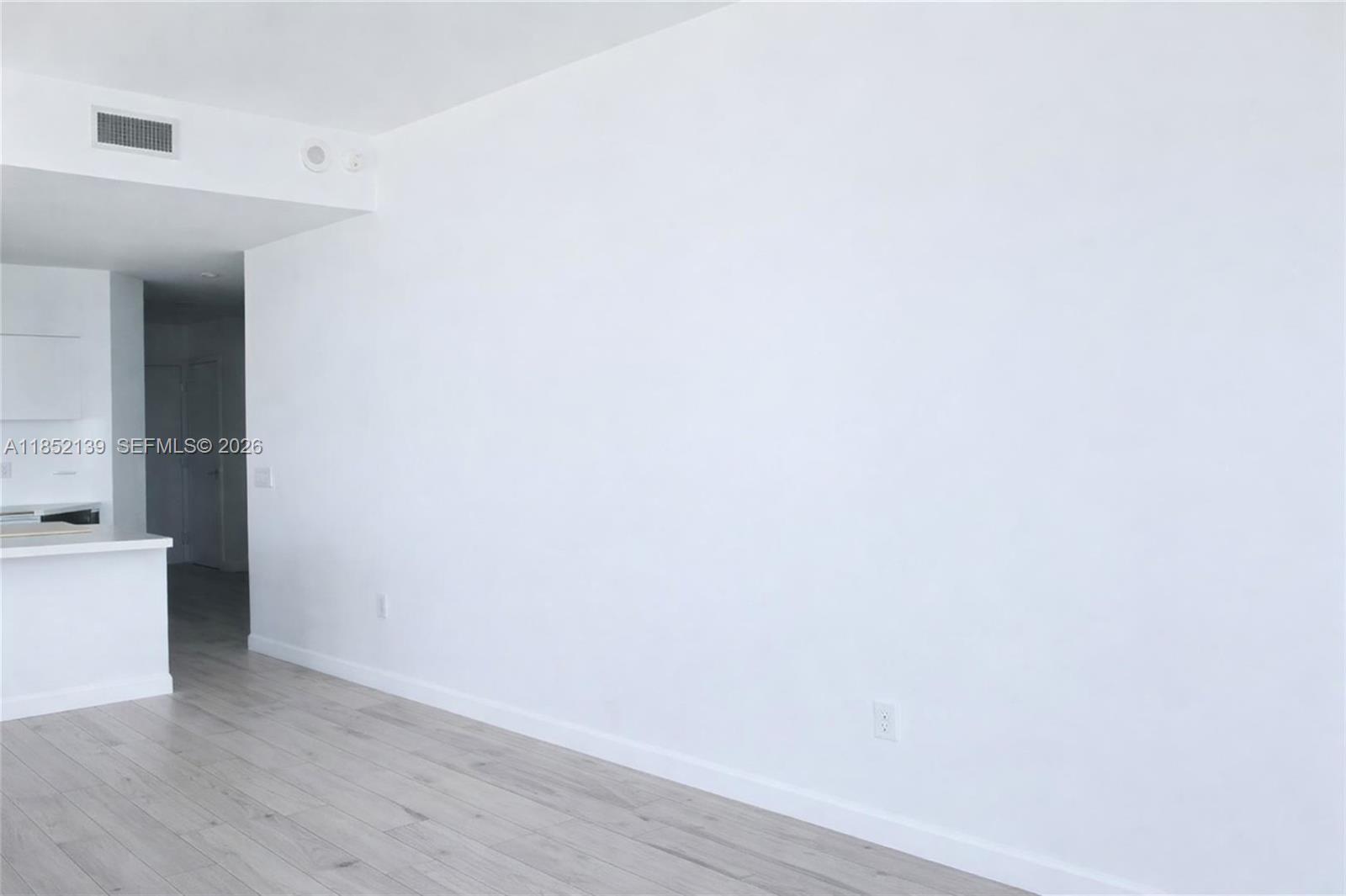 A white-walled room features light wood-look flooring and a doorway leading to a kitchen — 480 NE 31st St # 3301, Miami FL 33137, MIAMI, FL