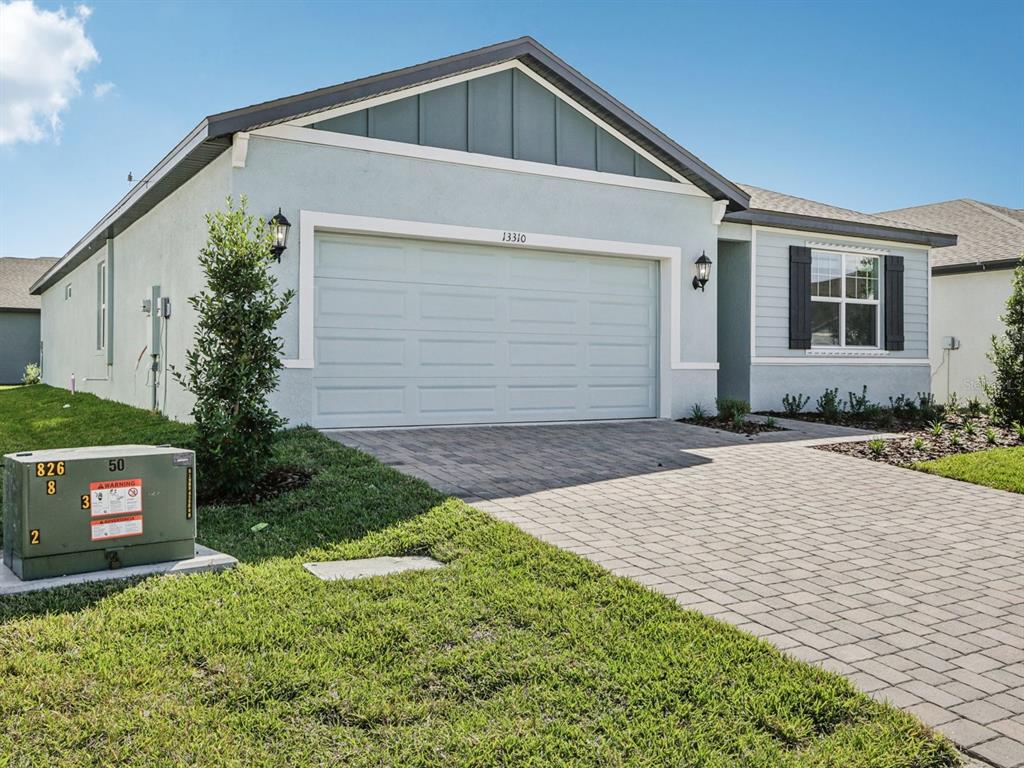 A single-story house with a light blue stucco exterior, a two-car garage, and a paver driveway — 13310 SHELLMORE AVENUE, PALMETTO, FL