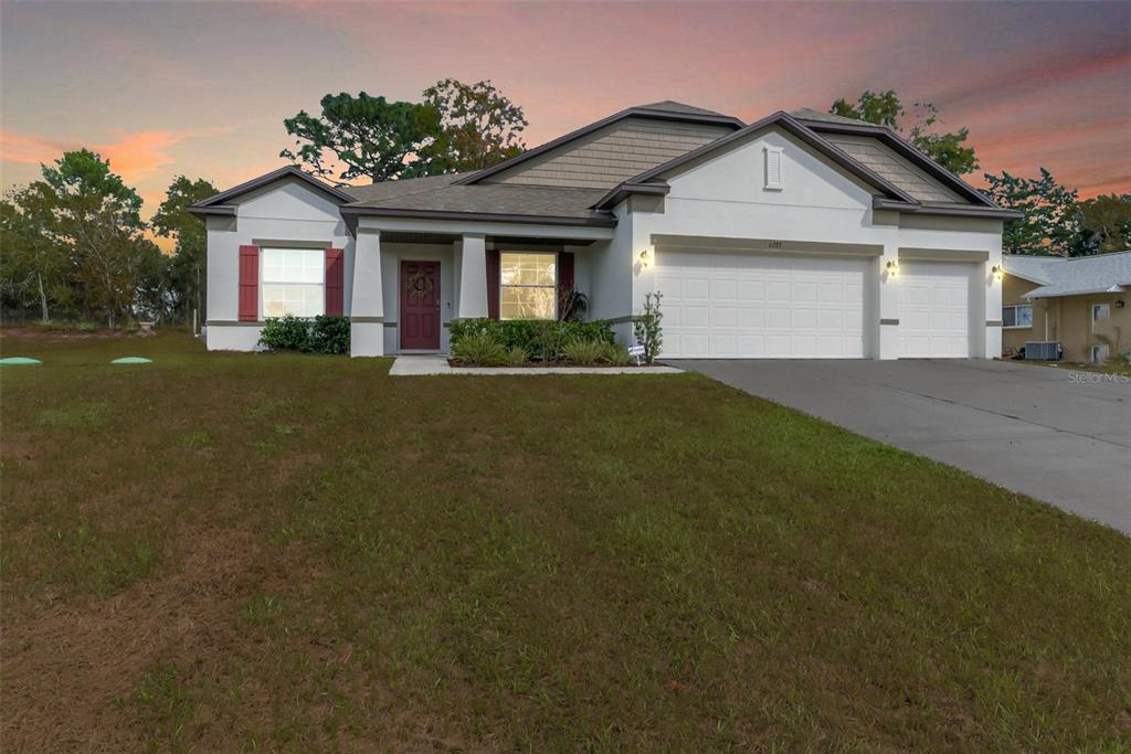 A single-story house with a white stucco exterior, red shutters, and a three-car garage — 6283 GRAPEWOOD ROAD, SPRING HILL, FL