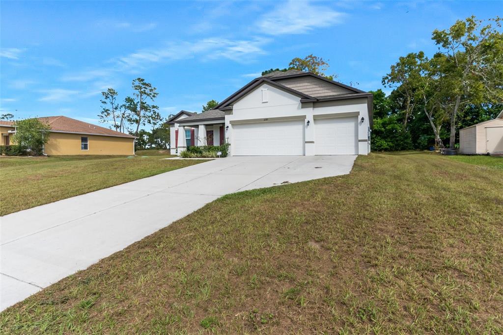 A single-story house with a white stucco facade, a three-car garage, and a concrete driveway — 6283 GRAPEWOOD ROAD, SPRING HILL, FL