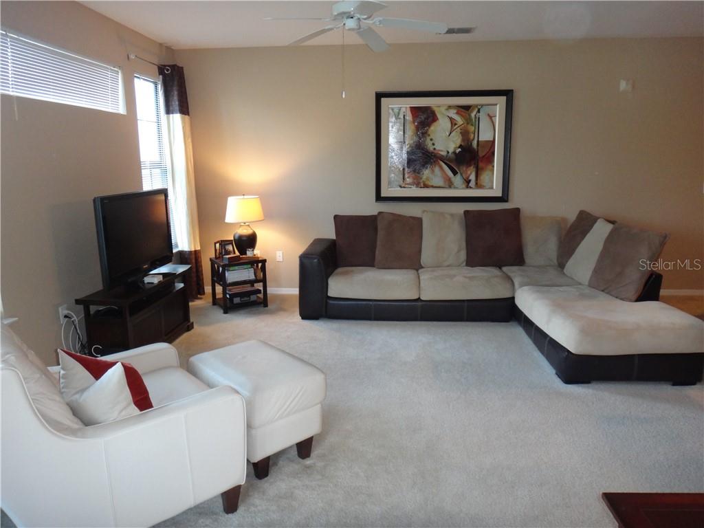 A living room features a sectional sofa, a white armchair with ottoman, and a television — 8325 38TH STREET CIRCLE E UNIT 102, SARASOTA, FL
