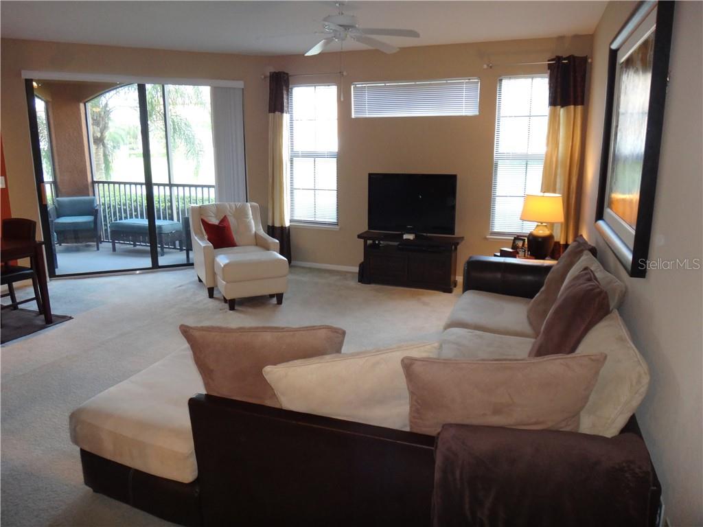 A living room with a sectional sofa, television, armchair, and a sliding door to a balcony — 8325 38TH STREET CIRCLE E UNIT 102, SARASOTA, FL