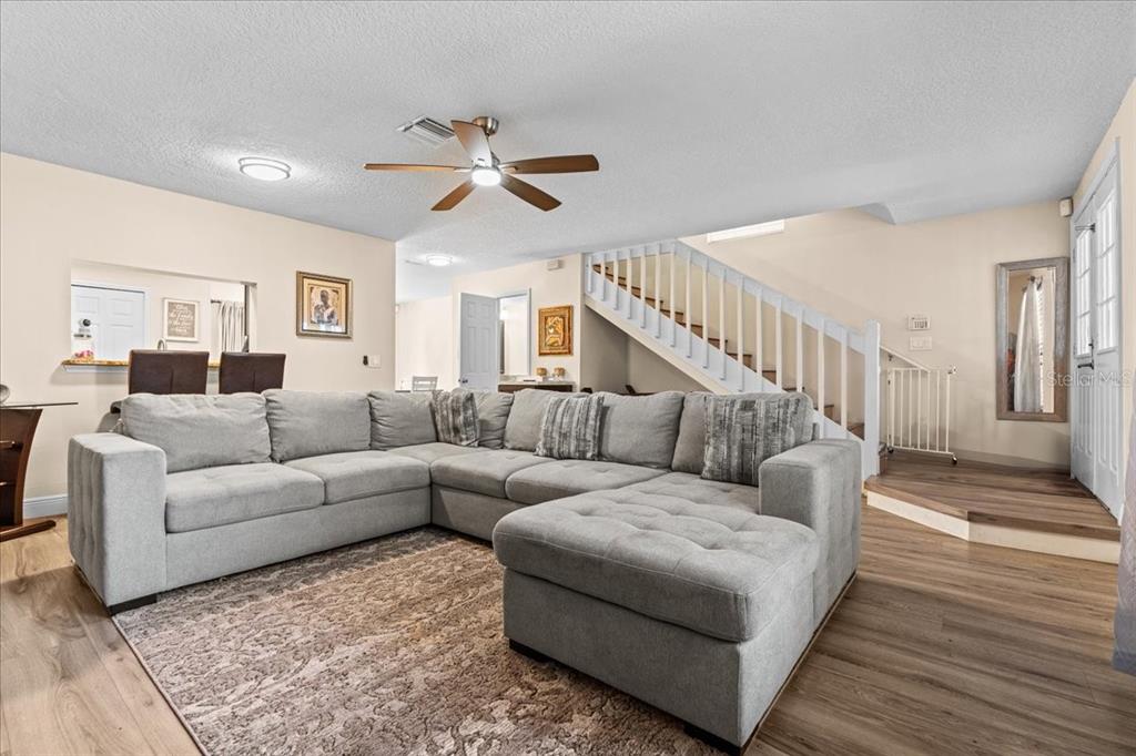A living room features a large grey sectional sofa, wood-look flooring, and a staircase — 5990 BRAEMAR PLACE UNIT 106, ORLANDO, FL