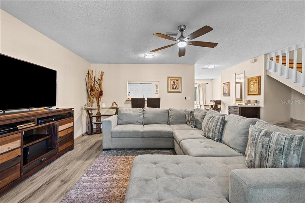 A living room features a large gray sectional sofa, a wooden media console, and stairs — 5990 BRAEMAR PLACE UNIT 106, ORLANDO, FL