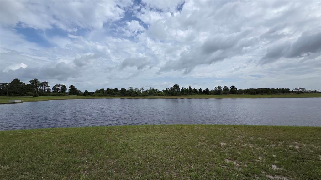 A wide view of a grassy lawn leading to a pond under a cloudy sky — 71 CEDAR CIRCLE E, LAKE WALES, FL