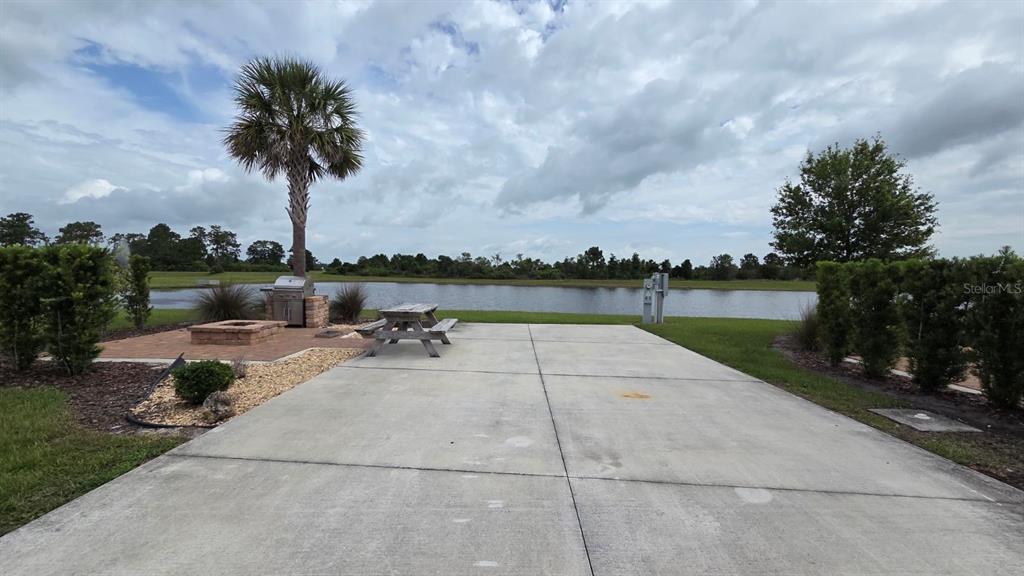 A concrete patio overlooks a lake with a picnic table, grill, and fire pit — 71 CEDAR CIRCLE E, LAKE WALES, FL