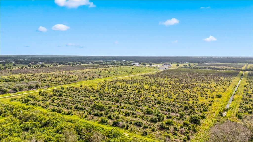 An aerial view shows a large, flat, rural field with scattered shrubs and a dirt path — FELLSMERE, FL