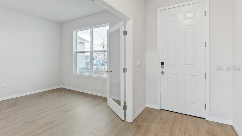 A room with light wood-look flooring and a glass-paneled door next to an entry door — 10436 WOODLAND GARDEN WAY, PARRISH, FL