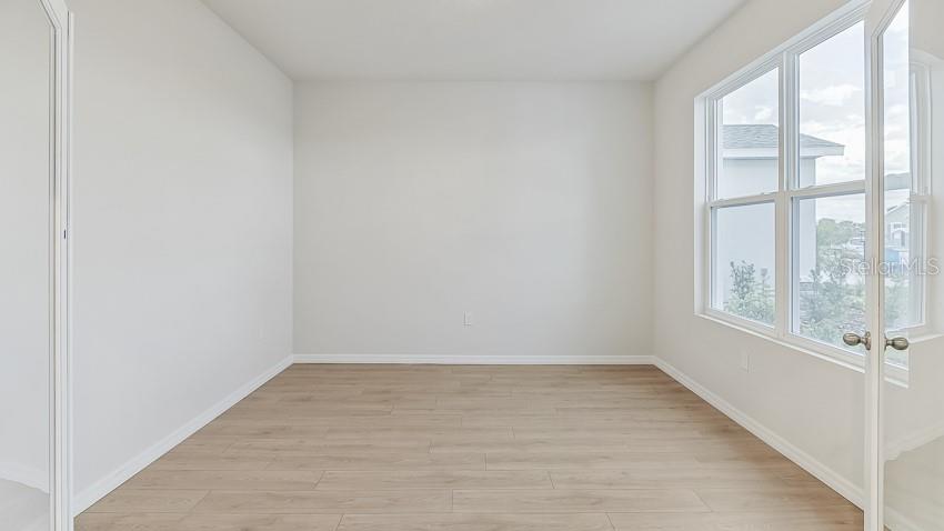 An empty room with light wood-look flooring, white walls, and glass French doors — 10436 WOODLAND GARDEN WAY, PARRISH, FL