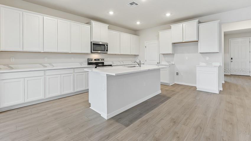 A modern kitchen features white cabinets, a central island, and light wood-look flooring — 10436 WOODLAND GARDEN WAY, PARRISH, FL