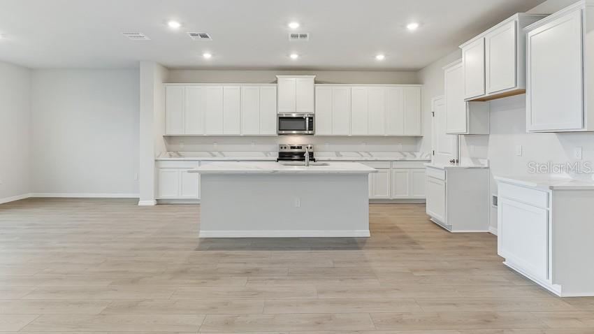 A bright kitchen features white cabinetry, a central island, and light wood-look flooring — 10436 WOODLAND GARDEN WAY, PARRISH, FL