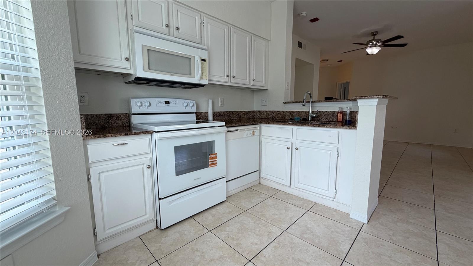 A kitchen features white cabinets, white appliances, granite countertops, and light-colored tile flooring — 23500 Walden Center Dr # 210, Estero FL 34134, ESTERO, FL