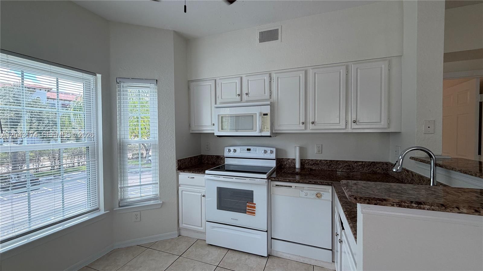 A kitchen features white cabinets, granite countertops, white appliances, and two windows with blinds — 23500 Walden Center Dr # 210, Estero FL 34134, ESTERO, FL