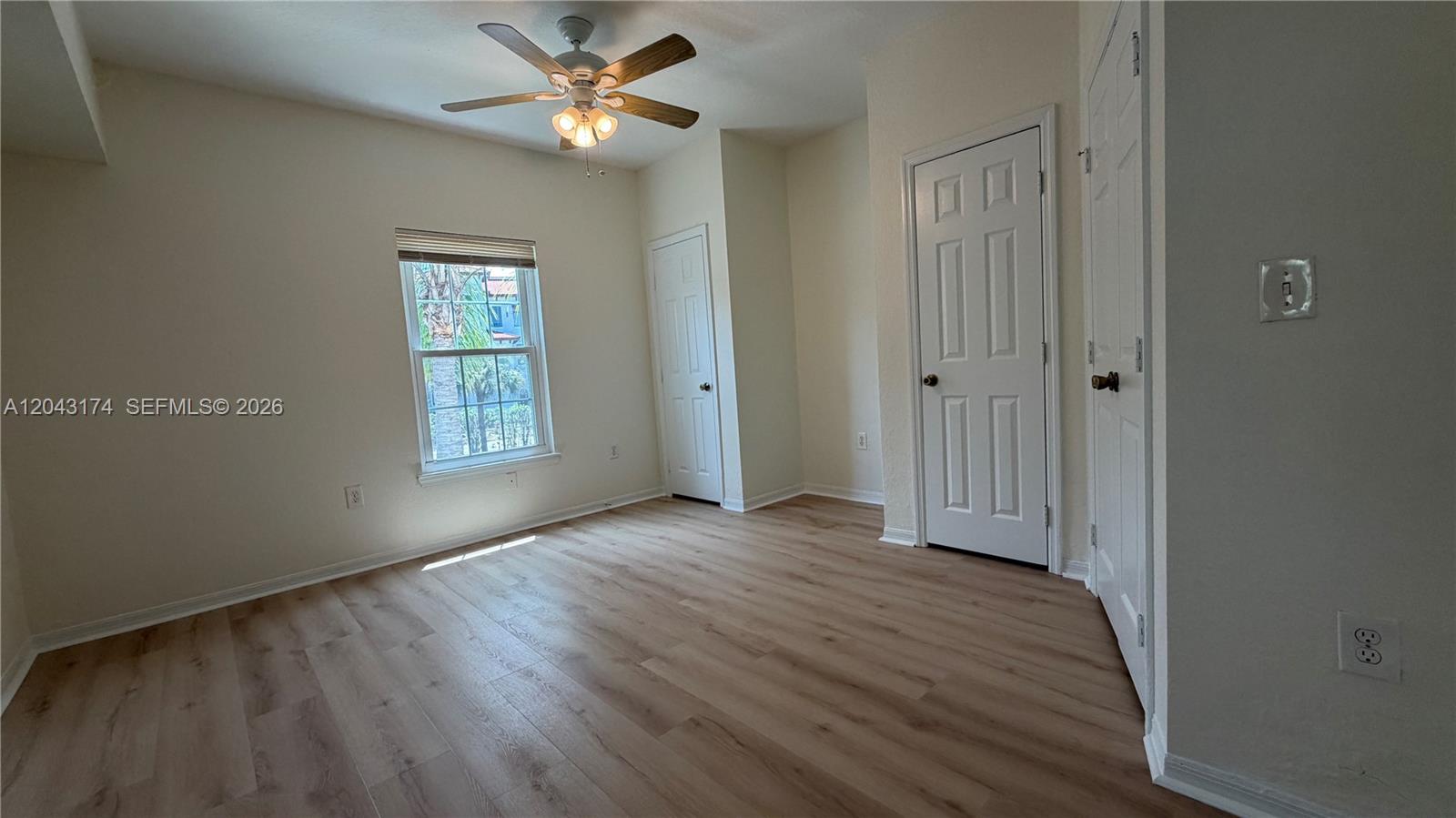 An empty bedroom features light wood-look flooring, a ceiling fan, and three white doors — 23500 Walden Center Dr # 210, Estero FL 34134, ESTERO, FL