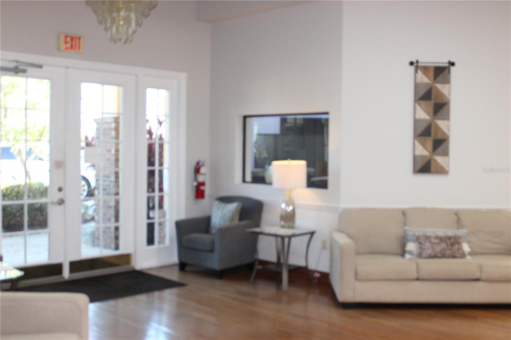 A lobby features a sofa, an armchair, a side table with a lamp, and glass doors — 4175 WOODLANDS PARKWAY UNIT 26, PALM HARBOR, FL