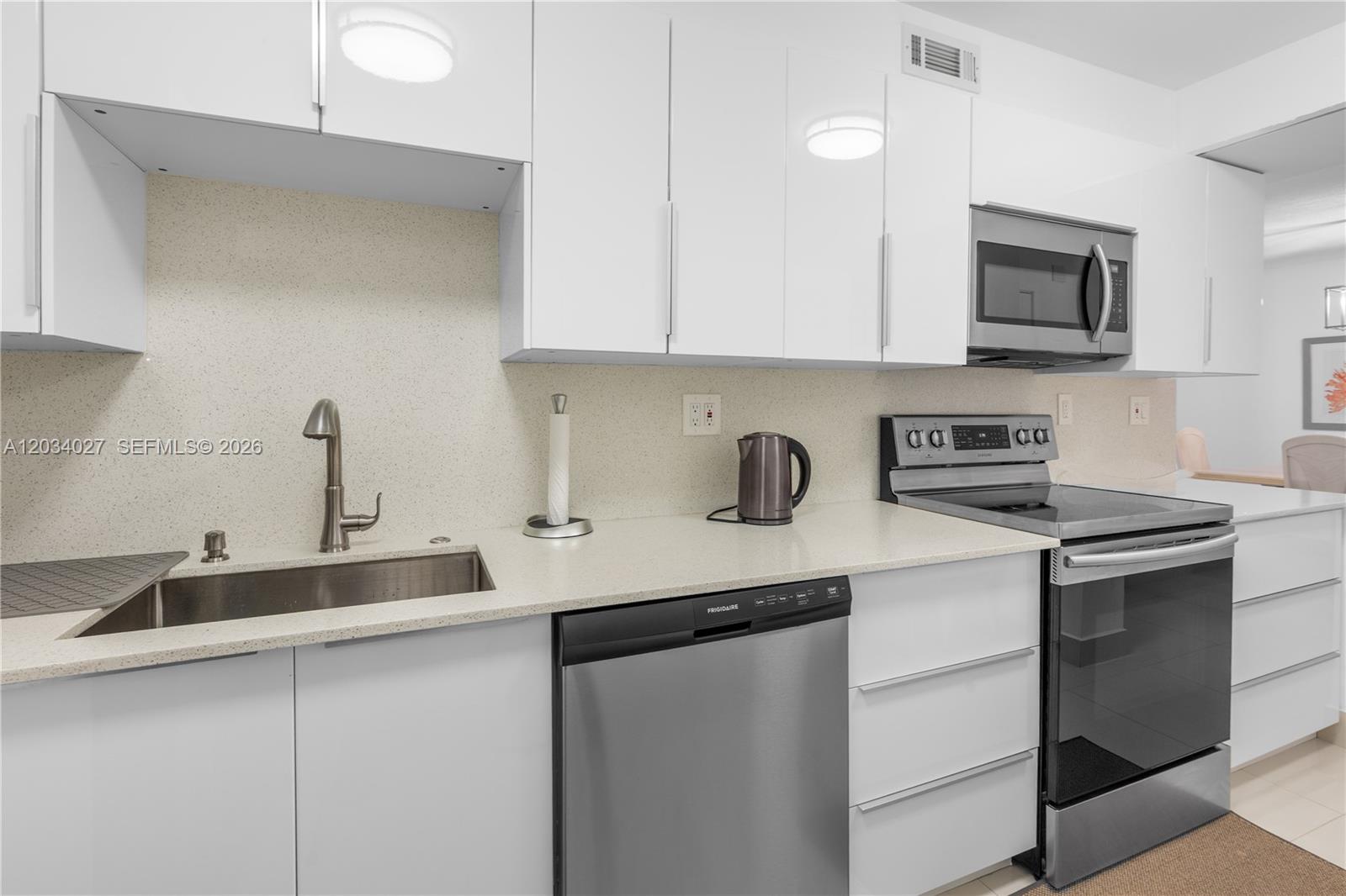 A modern kitchen features white cabinets, stainless steel appliances, and light-colored countertops — 1849 S Ocean Dr # 212, Hallandale Beach FL 33009, HALLANDALE BEACH, FL