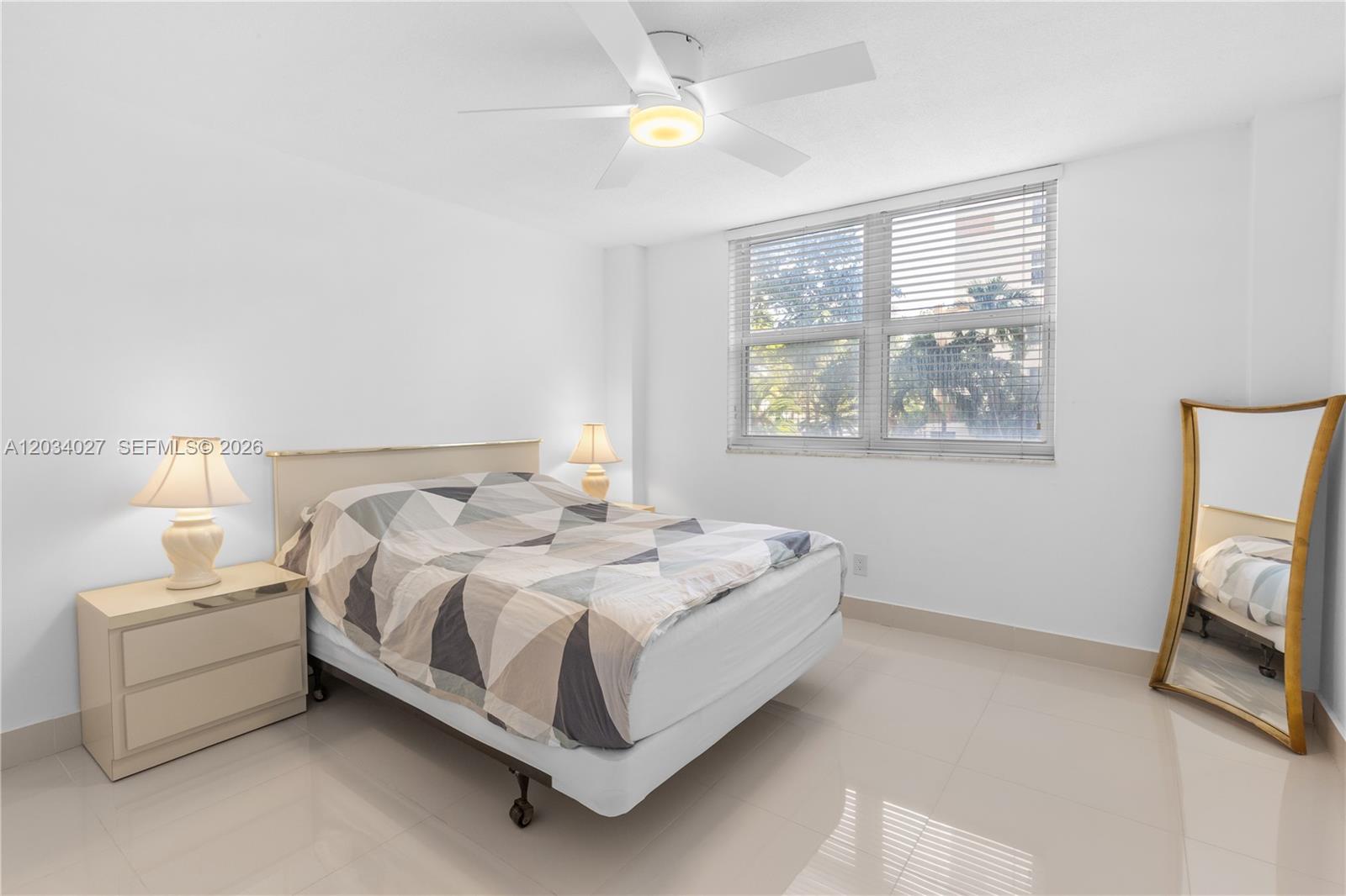 A bedroom features a bed with a geometric quilt, a ceiling fan, and a floor mirror — 1849 S Ocean Dr # 212, Hallandale Beach FL 33009, HALLANDALE BEACH, FL