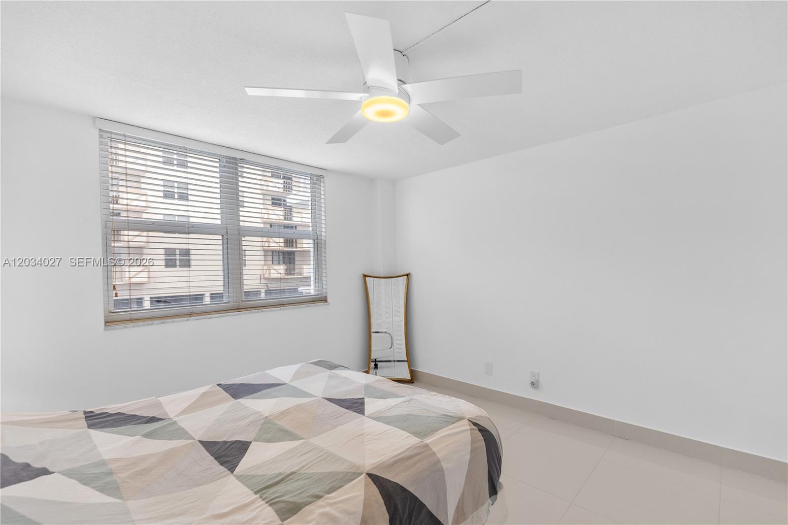 A bedroom features white walls, tile flooring, a ceiling fan, and a window with blinds — 1849 S Ocean Dr # 212, Hallandale Beach FL 33009, HALLANDALE BEACH, FL