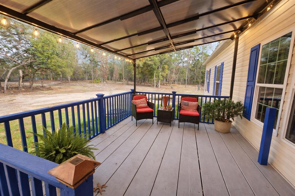 A covered wooden deck features blue railings, two chairs with red cushions, and string lights — 10630 NE 80TH STREET, BRONSON, FL