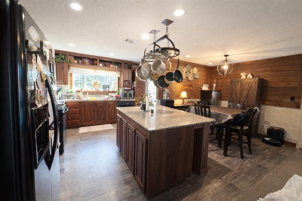 A kitchen features dark wood cabinets, a granite-topped island, and wood-paneled walls in the dining area — 10630 NE 80TH STREET, BRONSON, FL